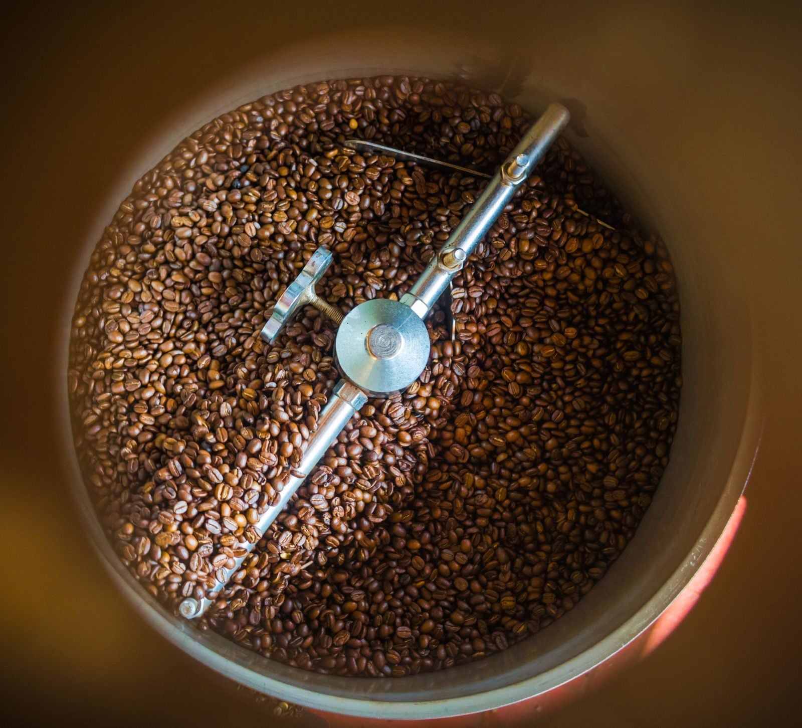 Looking down into a traditional manual roasting drum in Coorg, beans turning in amber light